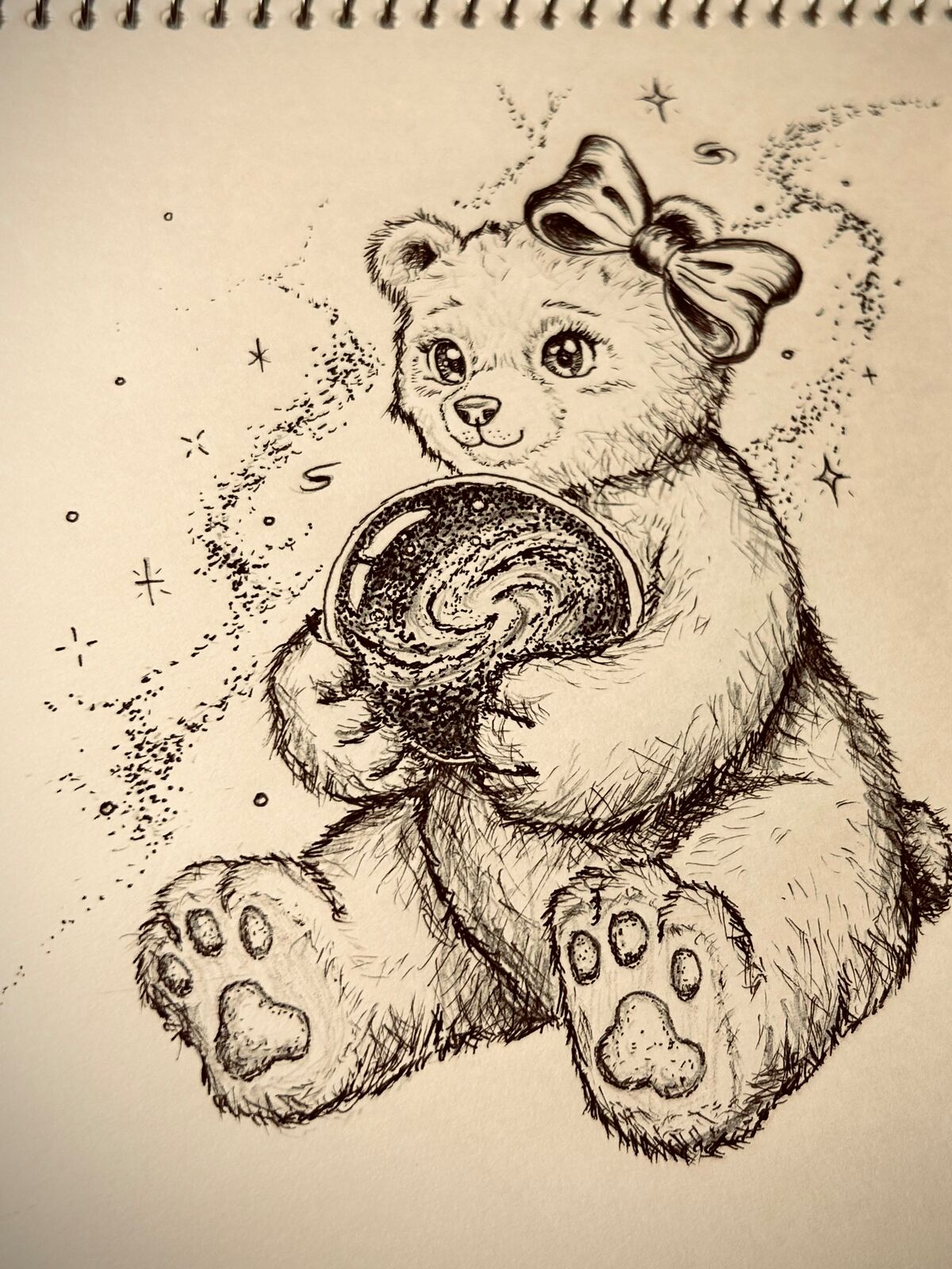 頭に大きなリボンをのせた、ふわふわの毛並みの子グマが、前足で渦巻き模様の銀河が入ったガラス玉を抱えて座っているイラスト。周囲には散らばった星ときらめきが描かれている。